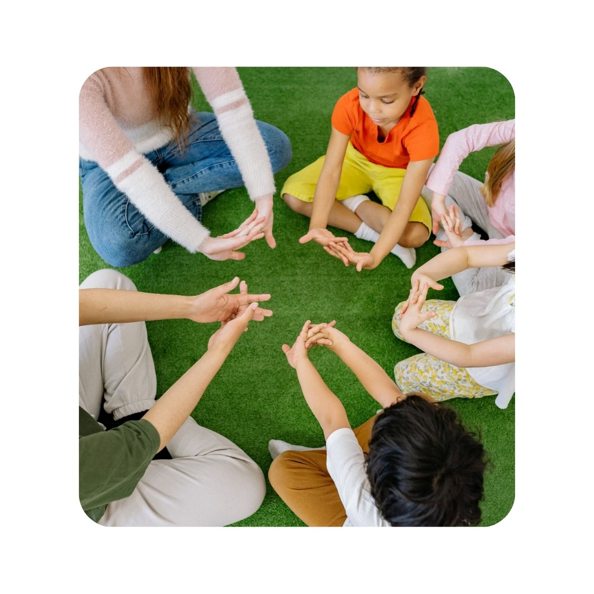 Children sitting in a circle with a teacher on grass with hands together